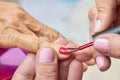 Manicurist applying red varnish to senior woman.