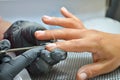 Manicurist in black gloves makes a cut manicure, trimming the cuticle on finger with a scissors Royalty Free Stock Photo