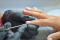 Manicurist in black gloves makes a cut manicure, trimming the cuticle on finger with scissors Royalty Free Stock Photo