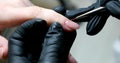 manicurist in black gloves paints nails in beige neutral color close-up beauty salon manicure process with gel polish