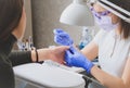 Manicurist in blue rubber gloves and medical mask make shape to the nail of a client with nail file