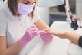 Manicurist in pink rubber gloves and medical mask applying nail polish to female nails