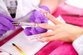 Manicurist wearing purple gloves placing artificial nail enhancements during a manicure treatment