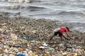 A man collecting plastic waste in a pile of garbage in the sea