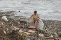 A woman collecting plastic waste in a pile of garbage in the sea