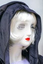 Female mannequin portrait with a white face, blond hair, long eyelashes, red lips and a black hood Royalty Free Stock Photo