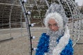 Mannequin of snow maiden in blue fluffy fur coat with white fringe standing on stone platform near arch with rows of lamps
