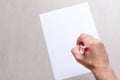 Mans hand with a ballpoint pen and blank white sheet of paper on a gray background, top view close-up