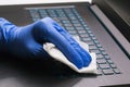 A mans hand in a blue glove cleans a laptop keyboard with an antibacterial agent to protect against the COVID-19 epidemic Royalty Free Stock Photo