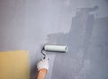 Mans hand in cloth glove with paint roller applies fresh paint and primer to wall surface. process of applying water-based paint