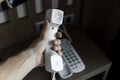 Mans hand holding handset of white vintage telephone with grey battoms on a brown table in hotel. Royalty Free Stock Photo