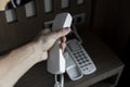 Mans hand holding handset of white vintage telephone with grey battoms on a brown table in hotel. Royalty Free Stock Photo