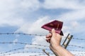 Mans hand holding a passport as a paper airplane over a barbed