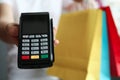 Mans hand holding pos terminal and many multicolored shopping bags closeup