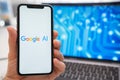 A mans hand holding a smartphone with Google AI neural network logo on the screen.