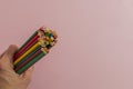 In a mans hand, a set of multi-colored pencils, turned the other way around, of different lengths on a light pink background in Royalty Free Stock Photo