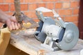 Mans hand sharpens a hoe on electric grindstone in rural shed