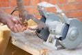 Mans hand sharpens a hoe on electric grindstone in rural shed