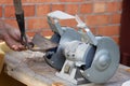 Mans hand sharpens a hoe on electric grindstone in rural shed