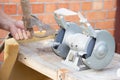 Mans hand sharpens a hoe on electric grindstone in rural shed