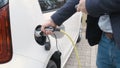 Mans hand unblocking an electric car with a key and diconnect a power cable supply plugged in the elctric vehicle.