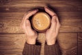 Mans hands holding a cup of coffee with foam over wooden table,