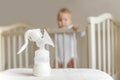 Manual breast pump and bottle with breast milk on the background of little baby in bed. Royalty Free Stock Photo