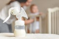 Manual breast pump and bottle with breast milk on the background of mother and baby near the baby`s bed.