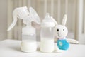 Manual breast pump, bottle with milk for baby and bunny toy over blurred background in children`s room. Royalty Free Stock Photo