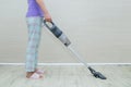 Manual gray vacuum cleaner in the hand of a standing Caucasian woman in home clothes. Vacuum the floor in room