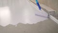 A worker paints the concrete floor with white paint. A worker paints the floor with a roller. Manual painting of a white floor