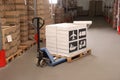 Manual pallet truck with stacked boxes with shipping icons and roll of stretch wrap in warehouse