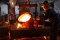 Industrial worker in protective gear pours molten metal at steel foundry. Manufacturing process in heavy industry with Royalty Free Stock Photo