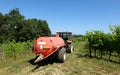 A manure tank spreader trailed by a tractor among vineyards in the hills