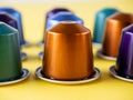 Many aluminum coffee capsules are displayed in a row on a yellow background. Food pattern. Capsules for the coffee machine