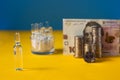 Many ampoules with vaccine and Ukrainian 100 hryvnia banknote and coins on a yellow-blue background. Medicine concept Royalty Free Stock Photo