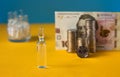 Many ampoules with vaccine and Ukrainian 100 hryvnia banknote and coins on a yellow-blue background. Medicine concept Royalty Free Stock Photo