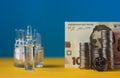 Many ampoules with vaccine and Ukrainian 100 hryvnia banknote and coins on a yellow-blue background. Medicine concept Royalty Free Stock Photo