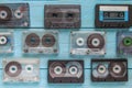 Many audio cassettes lie in a checkerboard pattern on a blue wooden background