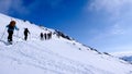 Many backcountry skiers traversing a mountain slope on their way to a high alpine mountain peak