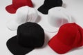 Many baseball snapback hats in different colors black, white and red laid out isolated on white surface