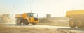 Many big articulated heavy industrial yellow dumper trucks driving on new highway road construction site on sunny day with blue