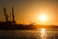 Many big cranes silhouette in the port at golden light of sunrise reflected in water. Berdiansk, Ukraine