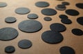 Many black circles of various sizes lay flat on beige textured board. Dark round shapes create abstract geometric pattern. Shows Royalty Free Stock Photo