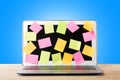 Many blank sticky notes covering modern laptop screen on wooden table against blue background. Concept of deadlines or ideas