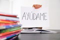 Many books, exercises books on the table and kid hand holding sheet of paper with Spanish word Auydame - Help me - Royalty Free Stock Photo