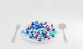 Many capsules of medicine are full of white plates with spoon and fork on a white background. The concept of taking medications or Royalty Free Stock Photo