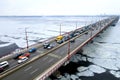 Many cars drive over river bridge in winter. Traffic jam at rush hour, air pollution, smog on highway, road. New bridge, Dnipro