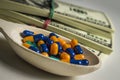 Many colored capsules in a wooden spoon on a table with packs of dollars Royalty Free Stock Photo