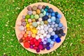 Many colorful balls, clews, wads, ravels of wool, laying in a large wooden bowl standing on the ground of green grass